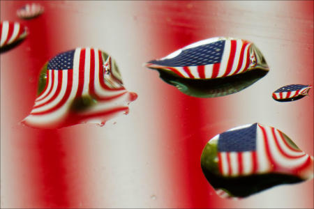 The American flag refracts through raindrops on a car windshield.
