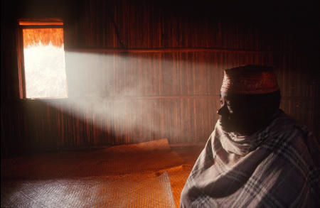 Namahoaka village leader, or Mpanzaka, Zafy Romain sits inside the Trano Be, or Big House, as smoke highlighted by morning light emerges through the window.